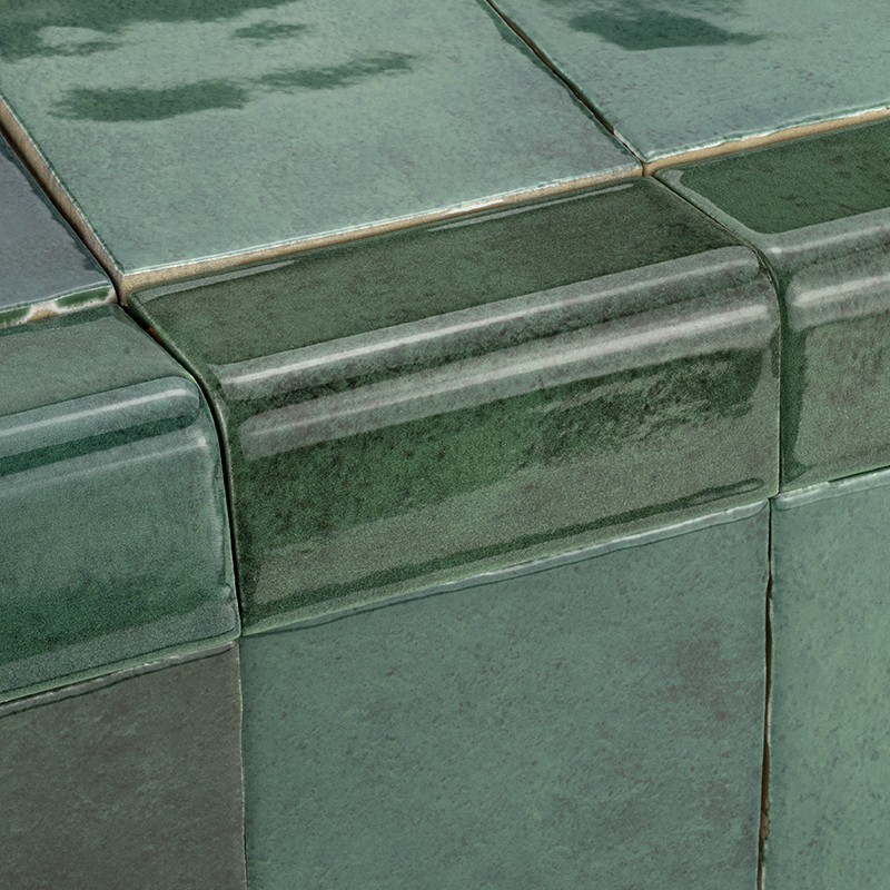 Azulejo cerâmico verde vidrado com borda arredondada formando um canto; juntas de rejunte finas e superfície brilhante com variações sutis de tonalidade.