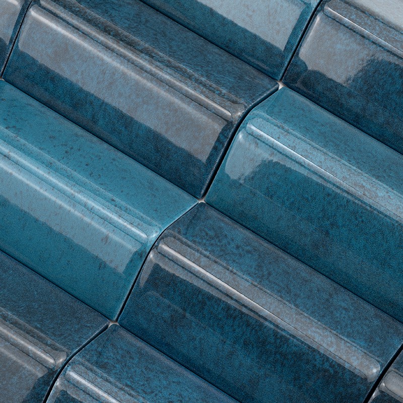 Azulejo cerámico curvado azul turquesa brillante; patrón de filas superpuestas formando relieves rectangulares con sombras y reflejos, aspecto esmaltado y textura ligeramente moteada.