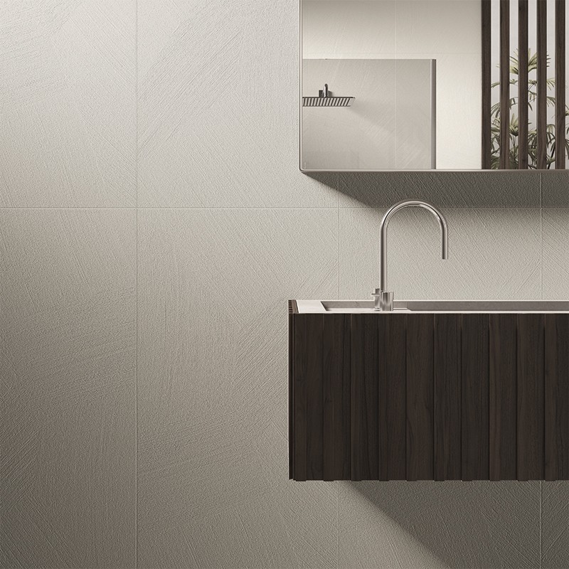 Carrelage mural clair texturé en grands carreaux, motifs obliques subtils — lavabo suspendu en bois foncé avec robinet chromé, miroir rectangulaire et claustra vertical laissant apparaître une plante.