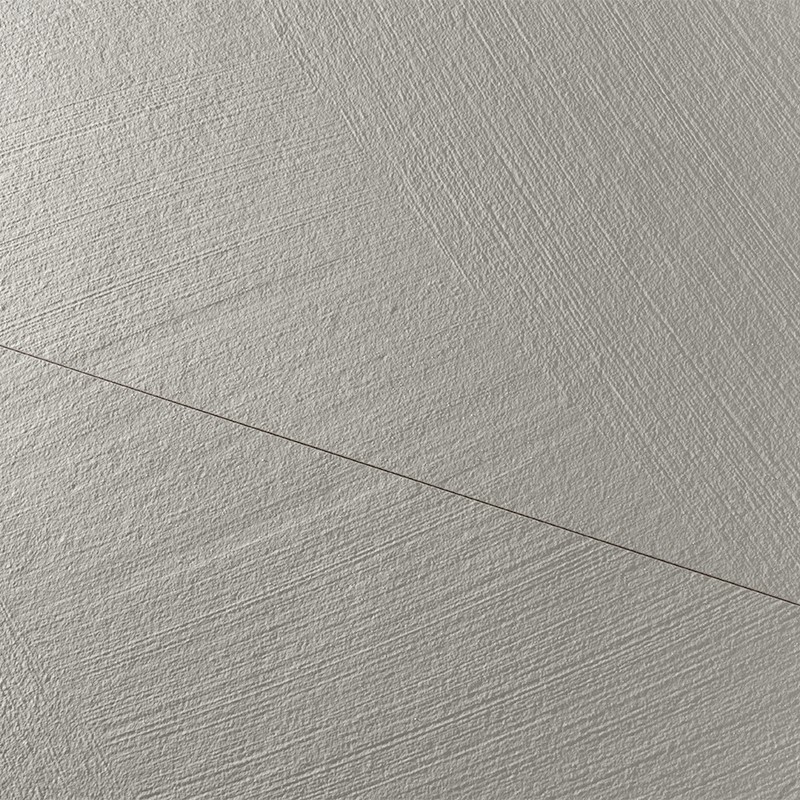 Azulejo claro con textura rugosa de líneas paralelas; línea diagonal oscura atraviesa la superficie; iluminación lateral crea sombras suaves; entorno no visible.