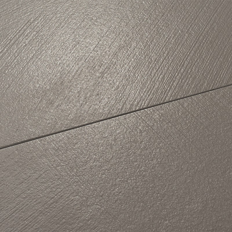 Azulejo gris texturizado con junta diagonal fina; superficie mate y rugosa que refleja luz tenue, en posible pavimento interior uniforme.