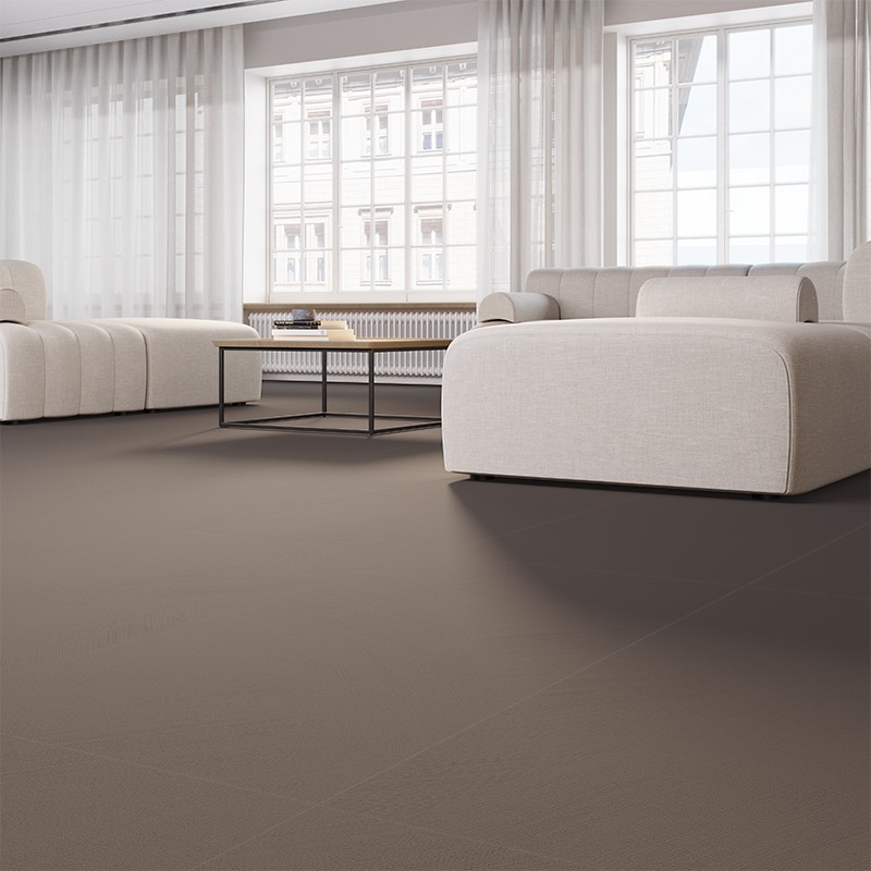 Wahrscheinlich großformatige, matte dunkelbraune Bodenfliese in hellem, modernem Wohnzimmer; zwei helle Polstersofas, niedriger schwarzer Couchtisch, große Fenster mit weißen Vorhängen, sichtbare Sockelleiste.
