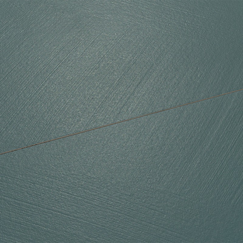 Blue-green tile with subtle concentric markings and matte sheen; thin dark diagonal line runs through the center on a uniform background.