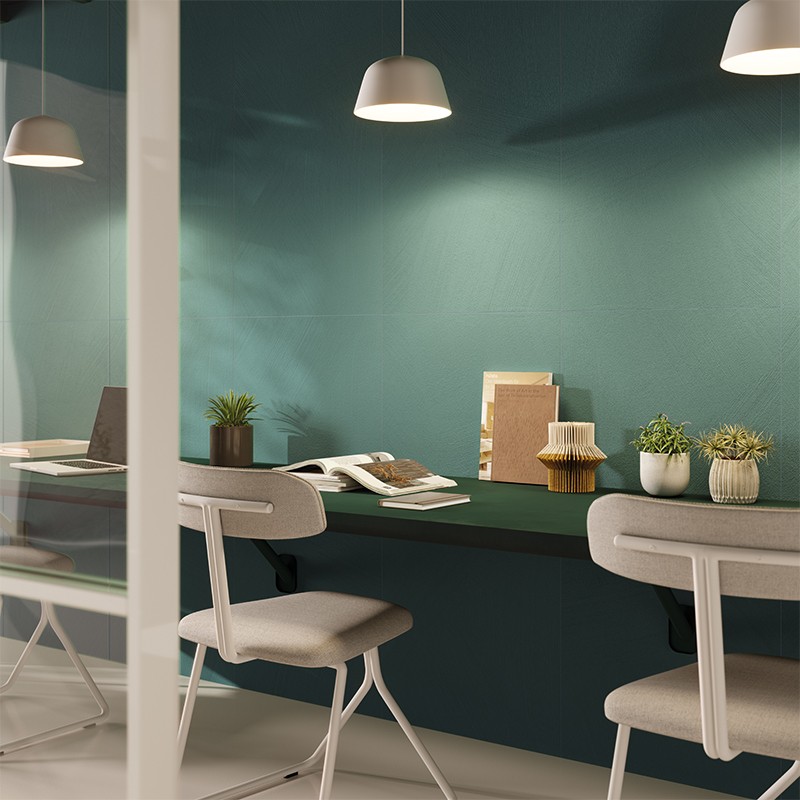 Dark green work surface in front of turquoise wall; three pendant lamps illuminate white chairs, potted plants and books stacked on the counter.