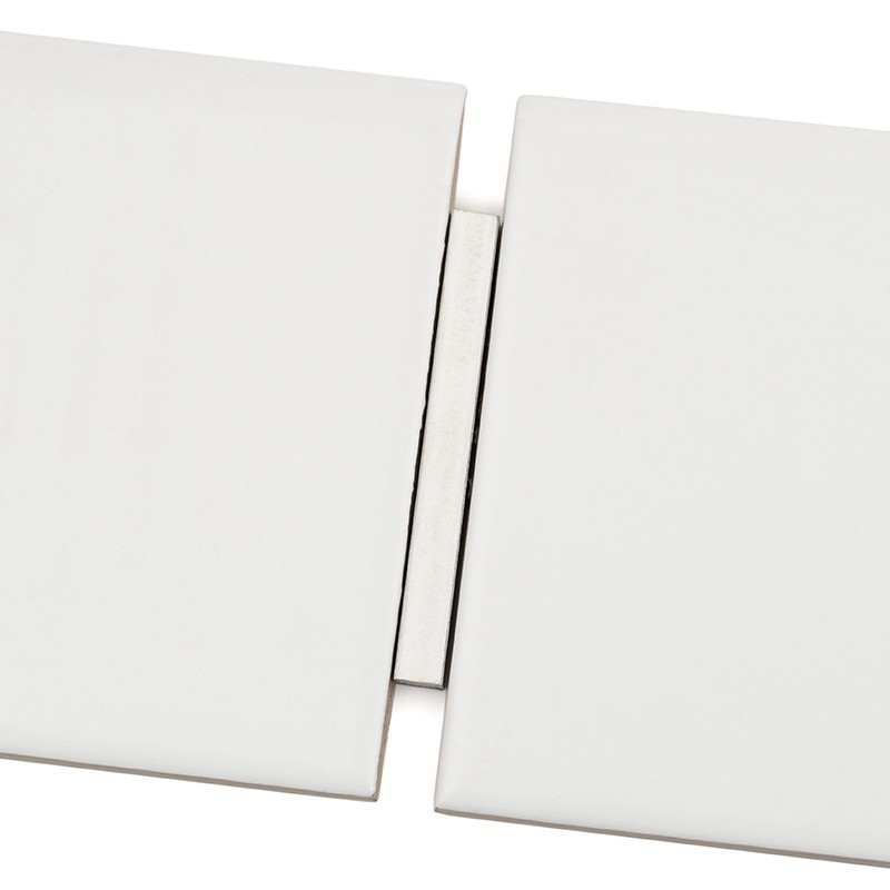Rectangular white ceramic tile as a focal point; central joint with a gray spacer between two adjacent pieces on a white background, smooth and matte surface.