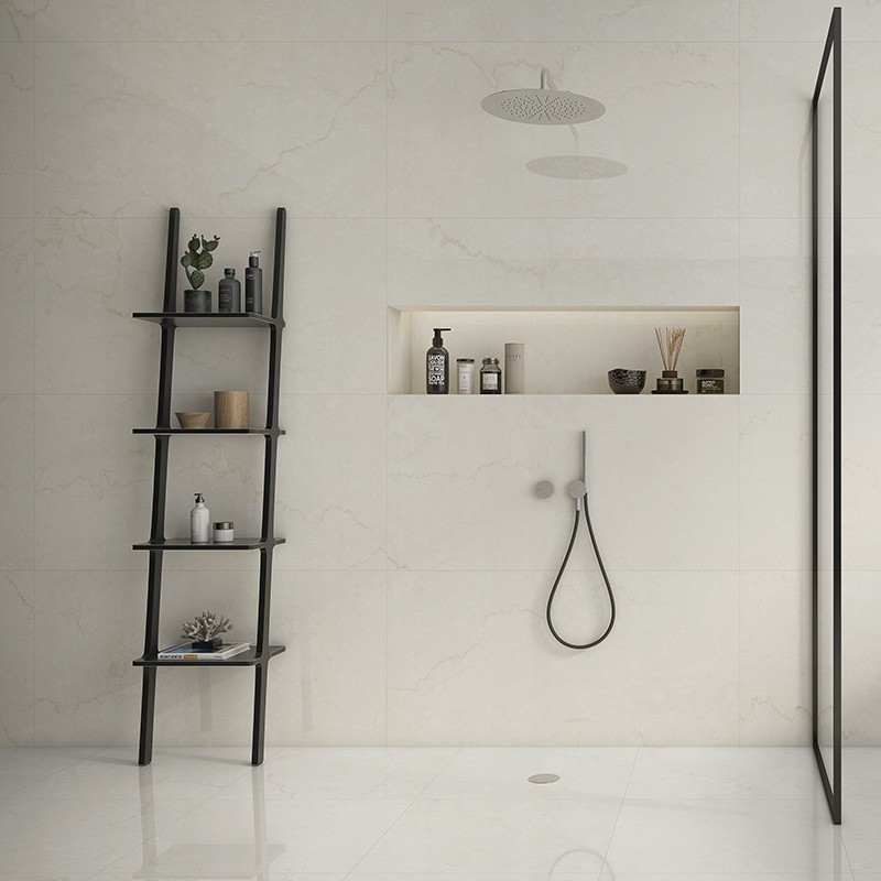 Große cremefarbene Wand- und Bodenfliese; Dusche mit Regenduschkopf, eingelassener Ablage mit Pflegeprodukten, schwarzes Leiter-Regal und Glas-Duschabtrennung.