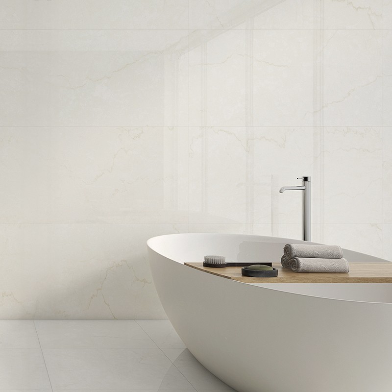 Cremefarbene Marmorfliese mit dezenter hellbrauner Aderung; Kontext: modernes Badezimmer mit freistehender ovaler Badewanne, Holzablage, aufgerollten Handtüchern und Wandarmatur.