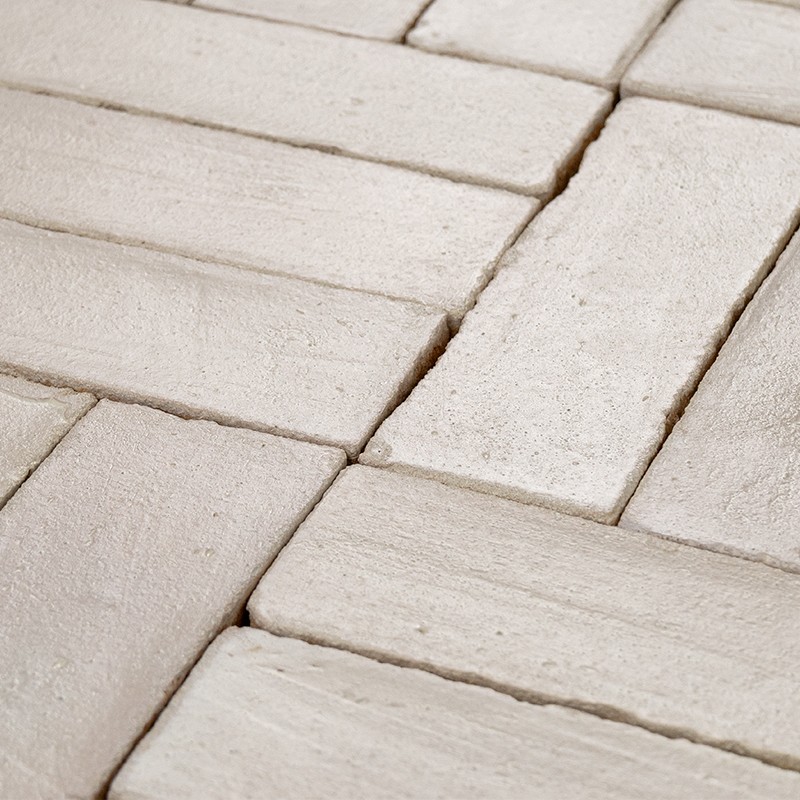Carrelage rectangulaire beige clair, plaquettes disposées en quinconce, surface légèrement texturée et joints profonds, aperçu rapproché du sol.