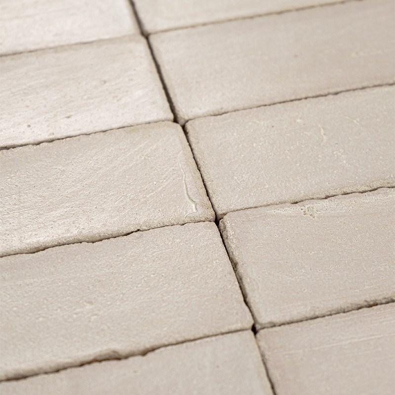 Matte beige rectangular tile; slightly rough surface with small imperfections; narrow joints with light grout forming a regular grid on a flat surface.