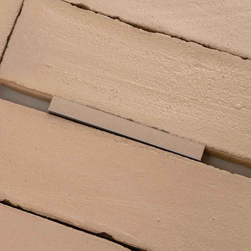 Azulejo rectangular beige texturizado; en la junta se observa una cuña plana colocada sobre la ranura, rodeado por otros azulejos similares alineados.