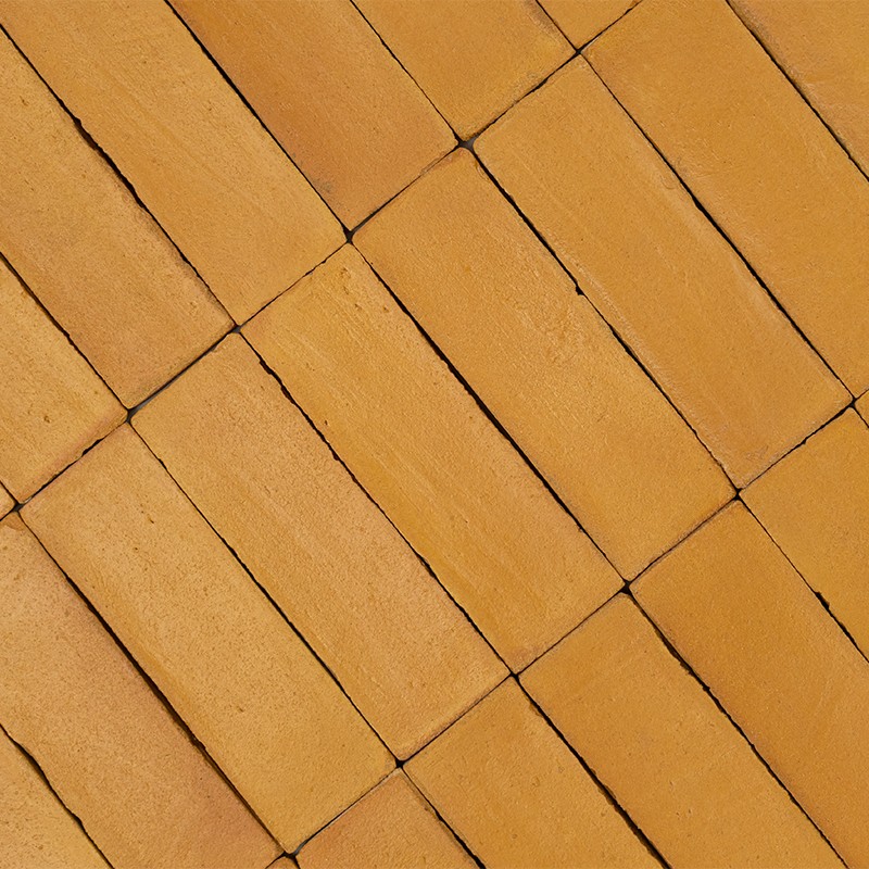 Azulejos retangulares ocre dispostos em padrão diagonal intercalado; juntas escuras definem ladrilho com superfície levemente rugosa, cobrindo toda a superfície visível.