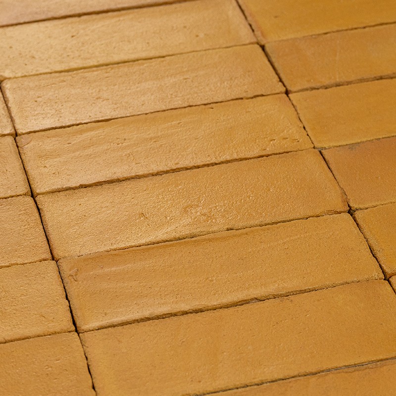 Rechthoekige terracottategels in warm oranjebruine tint, licht reliëf en zichtbare voegnaden, dicht opeengelegd in regelmatige rasterpatroon, close-up van vloer.