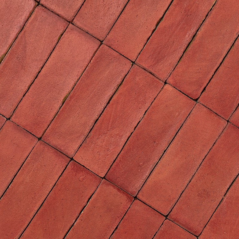 Carrelage rectangulaire rouge orangé posé en diagonale; joints étroits, fissures et traces de mousse entre les dalles.