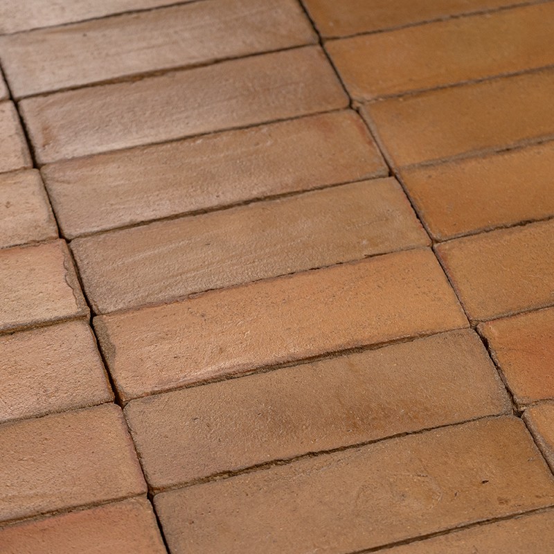 Azulejos retangulares terracota, com juntas visíveis e superfície levemente irregular, formando um piso rústico em tons de marrom-alaranjado.