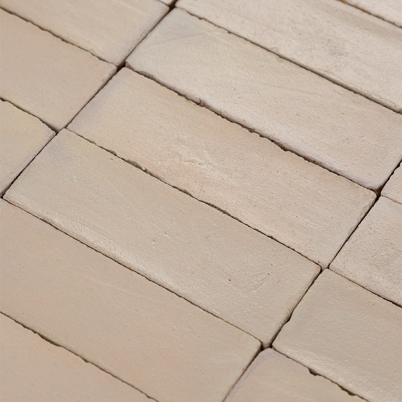 Rechteckige beige Fliesen mit sichtbaren dunklen Fugen und feiner Oberflächenstruktur, Nahaufnahme einer regelmäßig verlegten Kachelfläche.