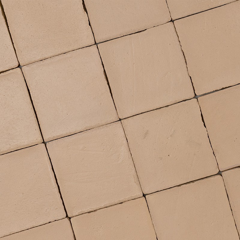 Azulejo cuadrado beige de superficie mate con microgrietas y juntas oscuras; varios azulejos alineados en cuadrícula, formando un revestimiento de pared o suelo.
