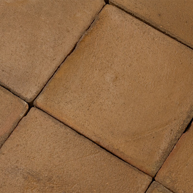 Beige, quadratische Betonfliese mit feiner Körnung und hellem, kreisförmigem Abriebstreifen; sichtbare Fugen und angrenzende ähnliche Fliesen, leicht schmutzig und gebraucht.