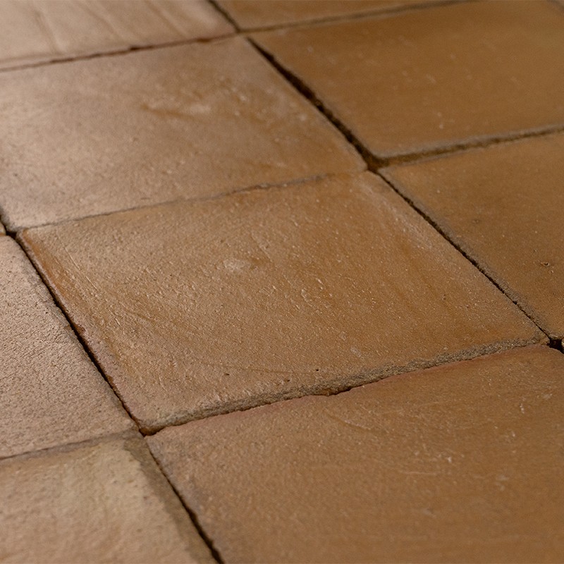 Azulejos quadrados de terracota, superfície levemente irregular e fosca, juntas escuras entre peças; piso rústico em tons quentes, visual próximo e detalhado.