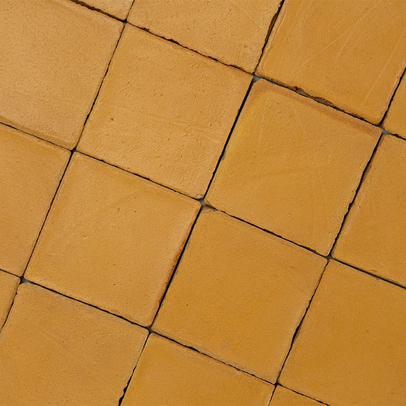 Yellow square tiles with a matte texture; dark, uneven joints form a slightly diagonal pattern on a continuous surface.
