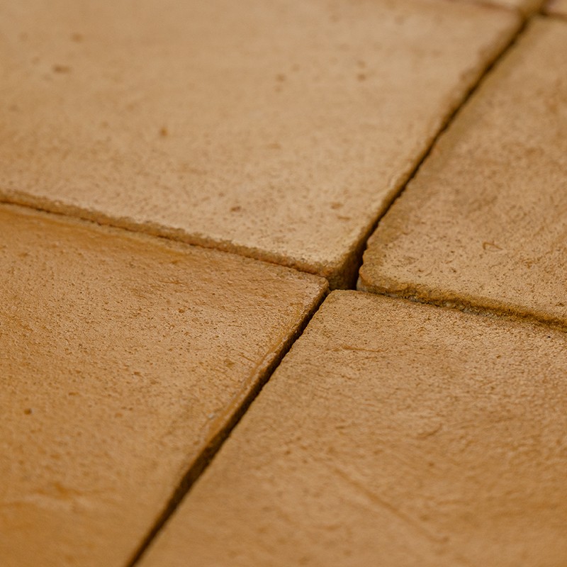 Square ceramic tiles in terracotta color; rough surface and microtexture, narrow joints forming a cross, light dirt in crevices, close framing.