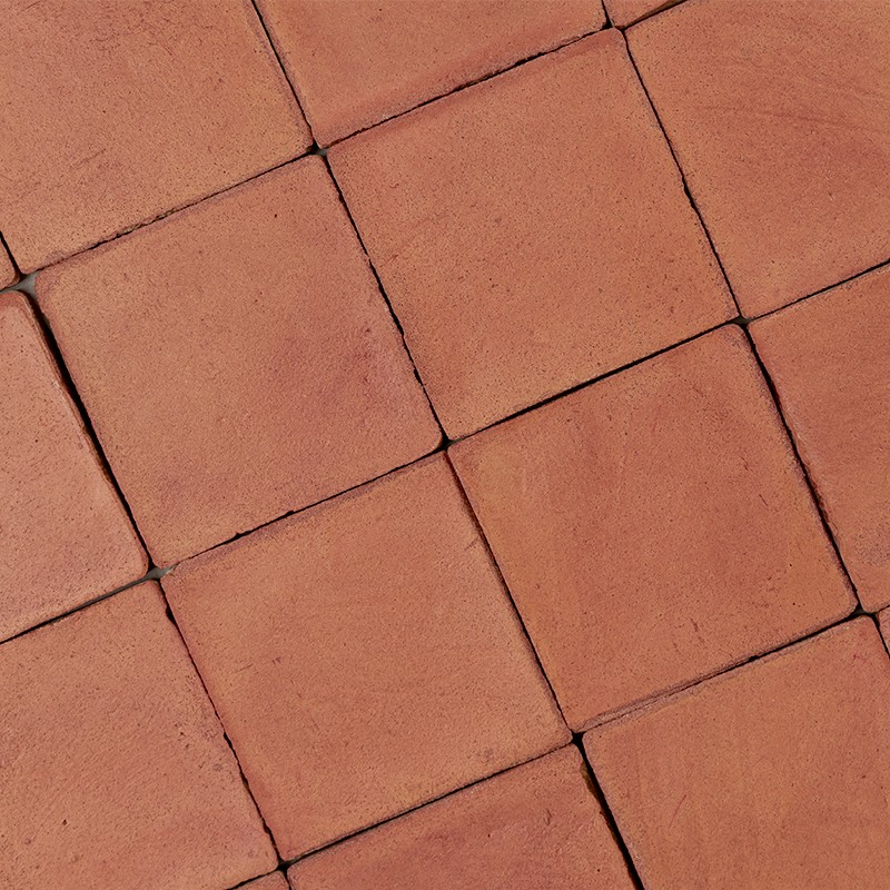 Vierkante terracotta tegels met zichtbare voegen, lichte kleurvariatie en kleine oppervlaktevlekjes, diagonaal gerangschikt op een vloer.