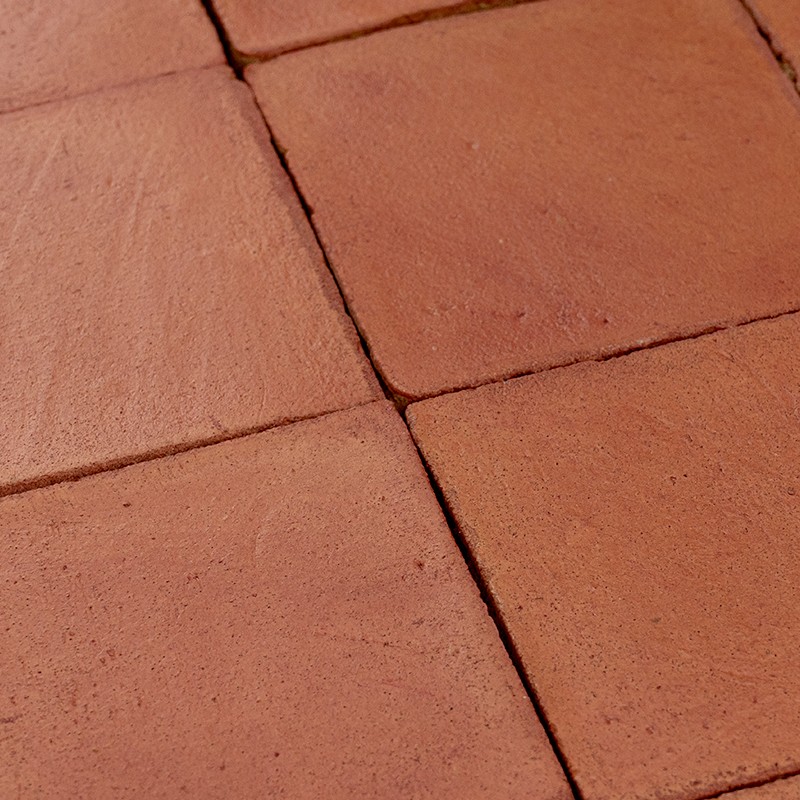 Square orange terracotta tile with matte surface and dark joints; group of four tiles in regular pattern, slightly misaligned edges.