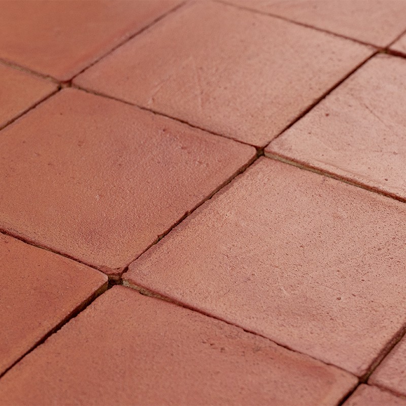 Terracotta vierkante vloertegels met zichtbare voegen en lichte slijtage, geplaatst in een regelmatig raster op een vloer.