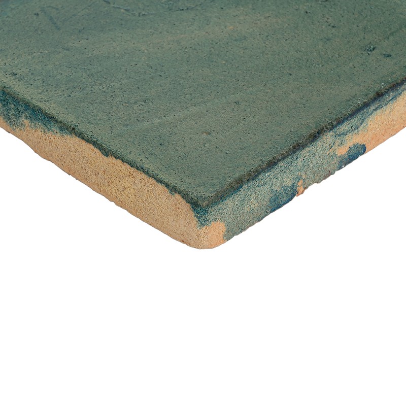 Azulejo retangular com superfície verde texturada e borda inferior bege exposta; canto superior esquerdo visível sobre fundo branco, mostrando espessura e leve desgaste.