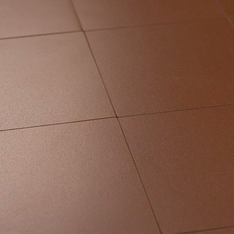 Quadratische matte rotbraune Bodenfliesen mit sichtbaren Fugen; leicht strukturierte Oberfläche, gleichmäßige Farbe, Nahaufnahme in neutraler Innenraumbeleuchtung.