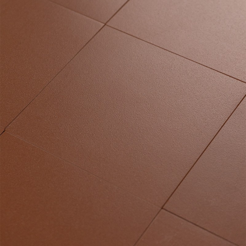 Carrelage brun terre cuite, dalles rectangulaires posées en léger décalage; surface mate légèrement granuleuse et joints fins visibles, vue rapprochée.