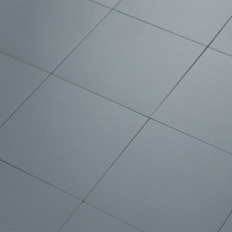 Carrelage gris mat composé de grandes dalles carrées aux joints fins, posé en quadrillage uniforme sur une surface plane, lumière douce créant légers reflets et ombres.