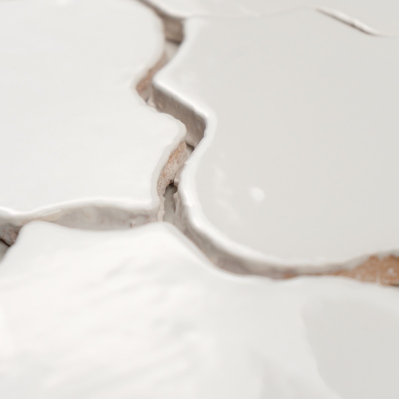 Carrelage blanc aux formes irrégulières et surfaces brillantes, joints de mortier beige visibles et légèrement fissurés, gros plan montrant textures et reliefs.