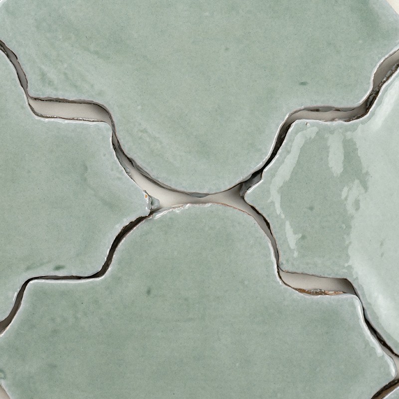 Pale green ceramic tiles of curved shape, joined in an interlocking pattern; joints and cracks visible with dust and small imperfections in the crevices.