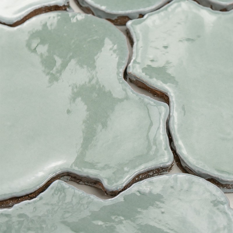 Azulejos cerâmicos verde-água com formas orgânicas interligadas; rejunte escuro entre peças, superfície vidrada brilhante refletindo luz.