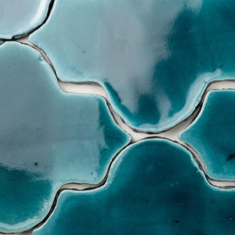Carrelage émaillé bleu-vert aux formes organiques, joints beiges dessinant des courbes; surface brillante avec reflets lumineux, texture lisse et nuances cyan et turquoise.