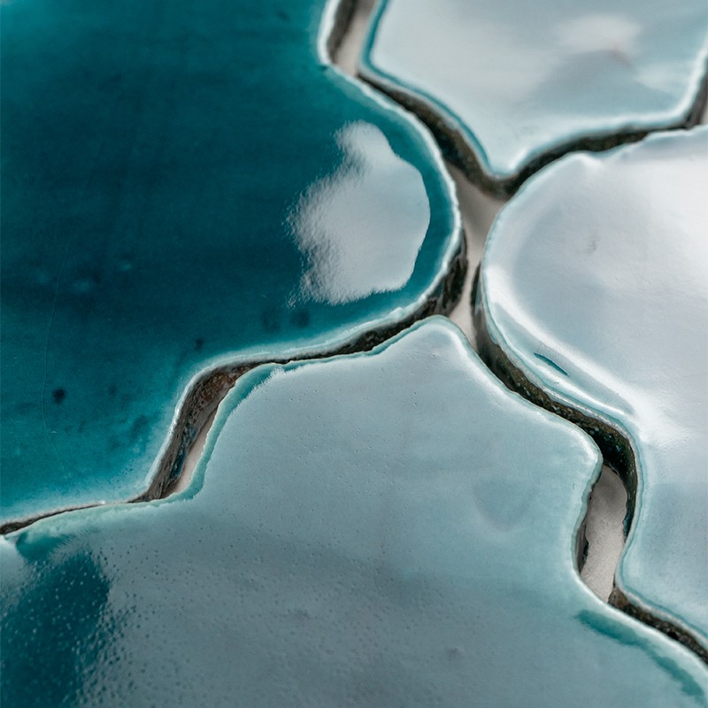 Carrelage émaillé (probablement céramique) aux pièces organiques bleu-turquoise et blanc, surfaces brillantes séparées par joints gris foncé; plan rapproché montrant texture et reflets.