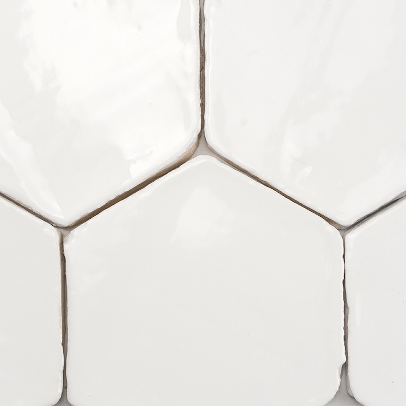 Azulejo hexagonal branco brilhante; rejunte cinza entre peças, superfície levemente irregular e reflexiva, encaixados formando revestimento de parede ou piso cerâmico.