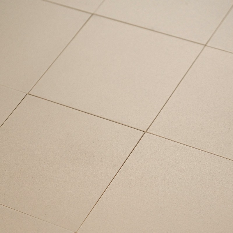 Azulejos quadrados bege claro alinhados por juntas finas; piso interior liso e levemente polido, iluminação suave realçando sombras discretas nas emendas.
