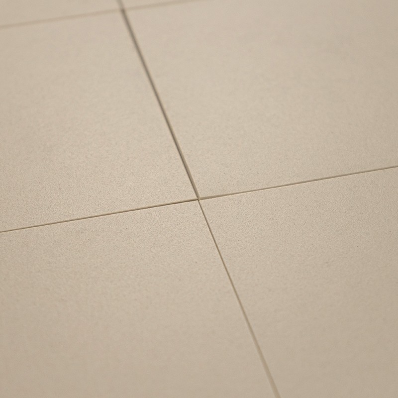Carrelage beige mat à surface légèrement granuleuse; joints fins formant une croix visible, quatre carreaux alignés en légère plongée.