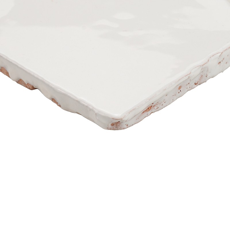Azulejo cerámico blanco esmaltado con bordes irregulares y pequeñas desconchaduras marrones; fotografiado en primer plano sobre fondo blanco limpio.