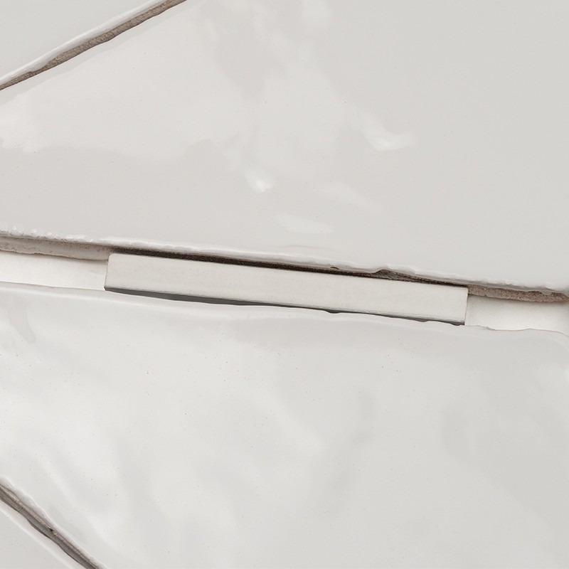 Irregular white tile with rounded edges and grayish joints; fits next to another tile separated by a thin rectangular piece, glossy surface with soft reflections.