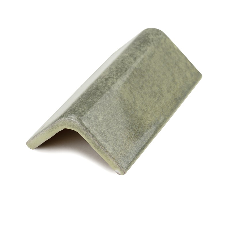 Azulejo remate en forma de L invertida, esmaltado verde grisáceo con textura marmoleada; colocado sobre fondo blanco aislado con sombra suave debajo que indica ligero levantamiento.
