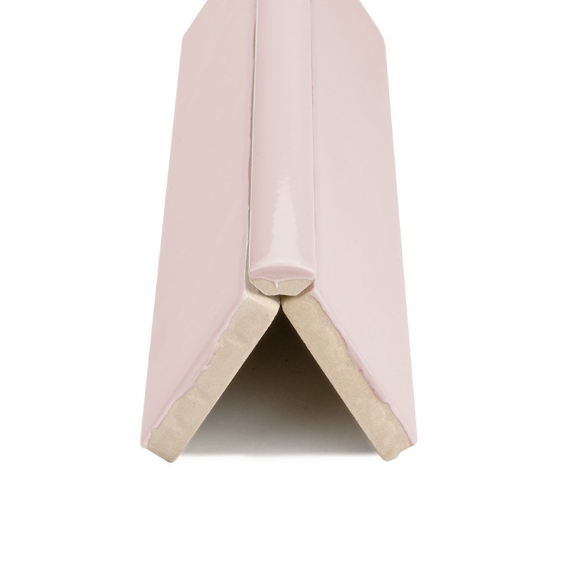 Azulejo angular esmaltado rosa pálido, sección en V con borde no esmaltado beige; pieza para esquinas, colocada sobre fondo blanco neutro.