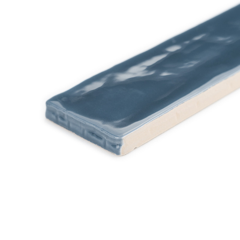 Un azulejo cerámico azul rectangular con una superficie brillante refleja la luz. Se apoya sobre un fondo blanco liso.