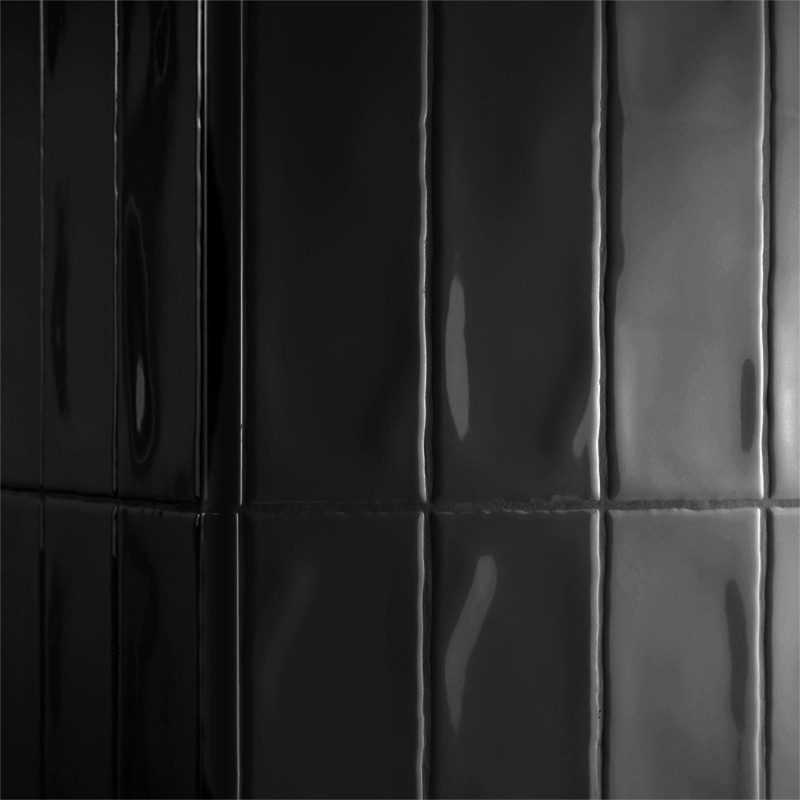 Los azulejos negros brillantes reflejan la luz verticalmente, creando una superficie elegante y moderna en un espacio minimalist