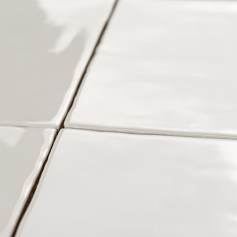 Cuatro azulejos de cerámica blanca brillante forman una cuadrícula, unidas por finas líneas de lechada, que reflejan la luz en u