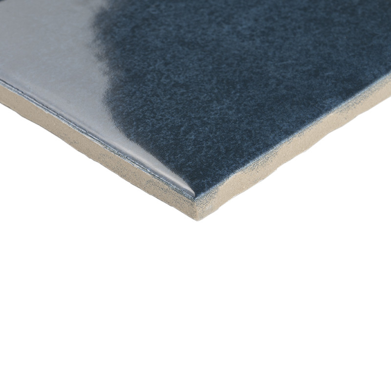 Azulejo cerámico azul oscuro con acabado brillante en esquina, núcleo beige visible; fondo blanco neutro que lo aísla.