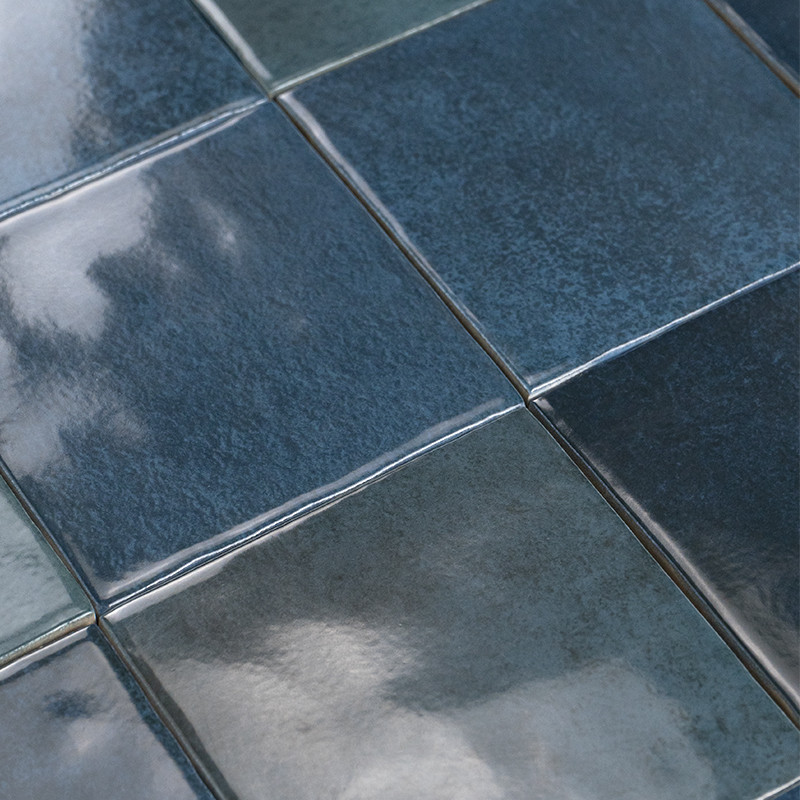 Azulejo cerámico azul oscuro con acabado brillante; colocado en matriz cuadrada junto a otros, con juntas finas y superficies reflectantes que muestran reflejos difusos.