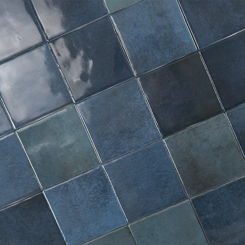 Azulejos cuadrados esmaltados azul oscuro dispuestos en patrón diagonal formando un mosaico; juntas claras; superficie brillante con ligero reflejo y variación de tono.