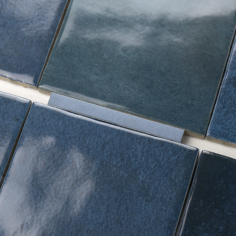 Azulejo esmaltado azul oscuro, superficie brillante con sutiles variaciones tonales; dispuesto junto a otros azulejos similares con juntas blancas visibles en un primer plano.